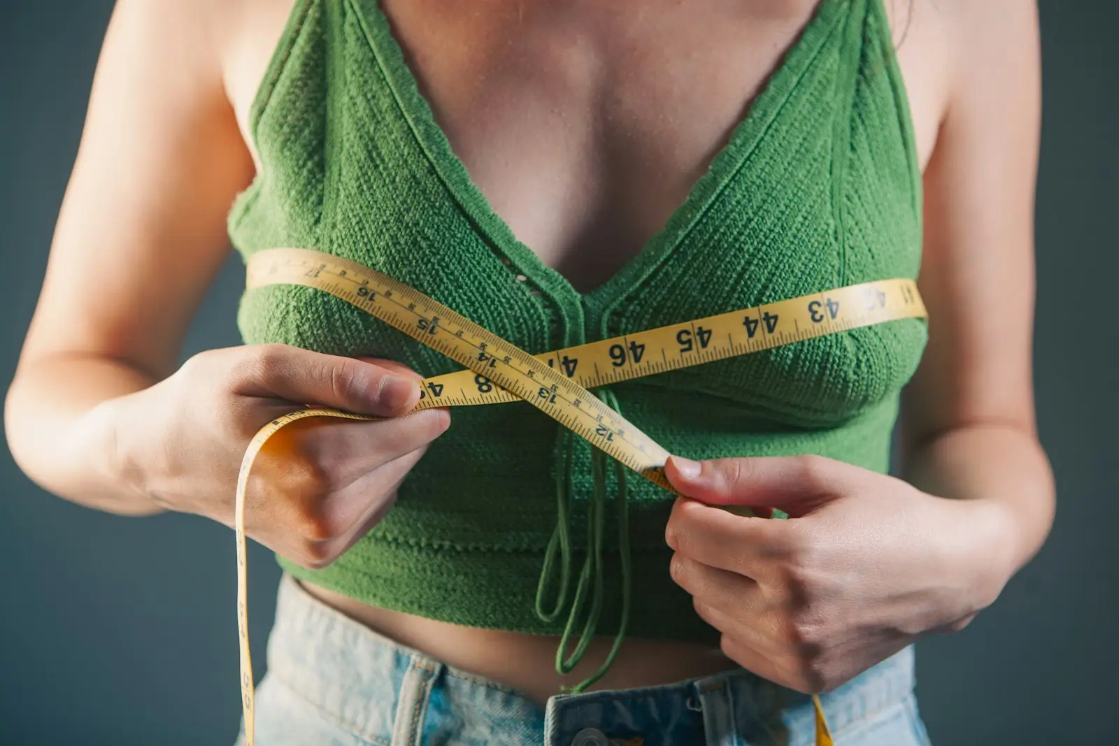 A woman measuring around her bust with a yellow tape measure