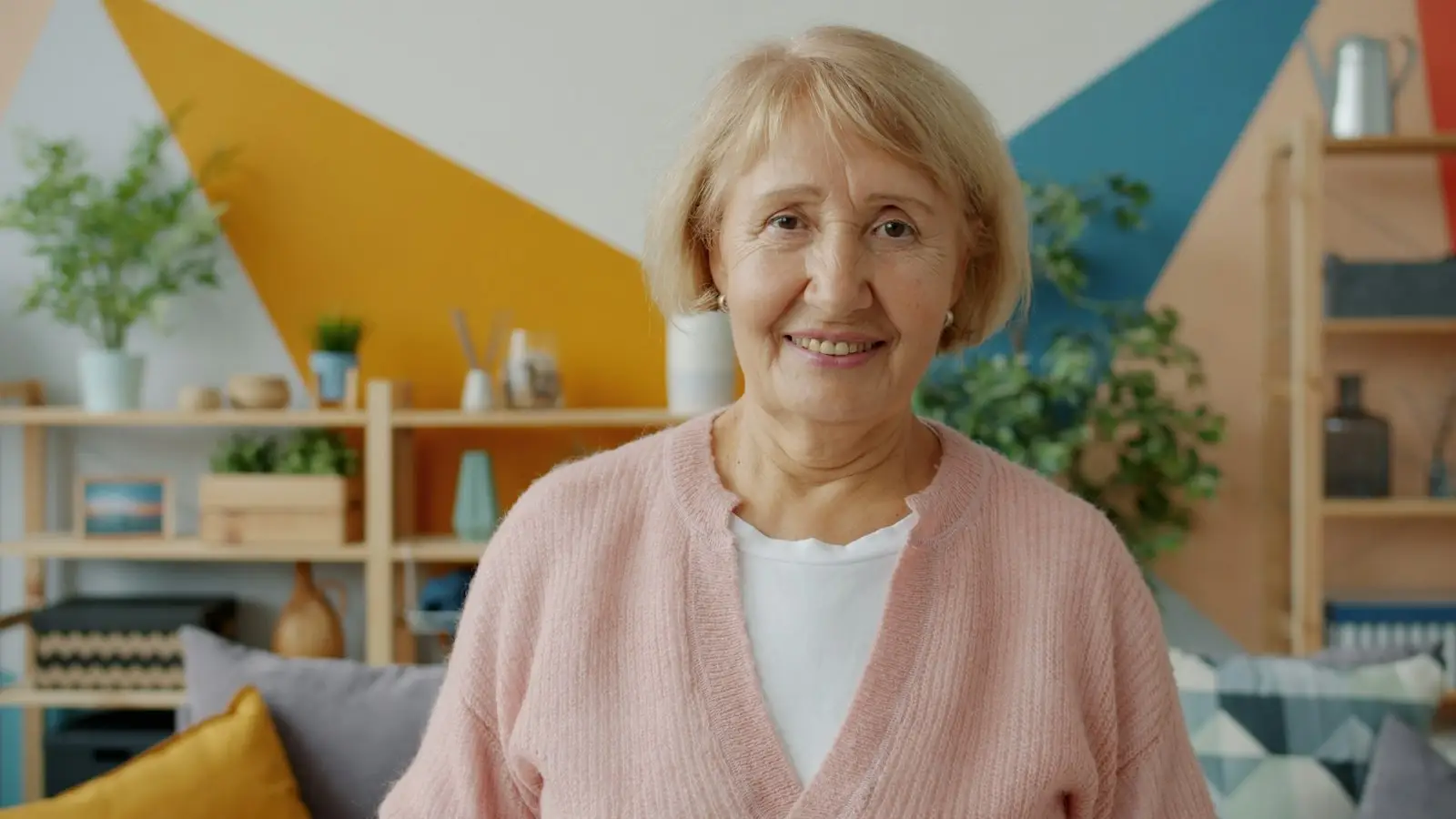 A smiling older woman in a pink cardigan at home