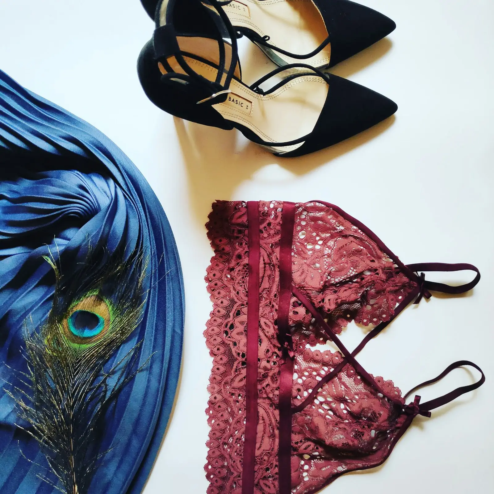A burgundy lace bralette beside a peacock feather