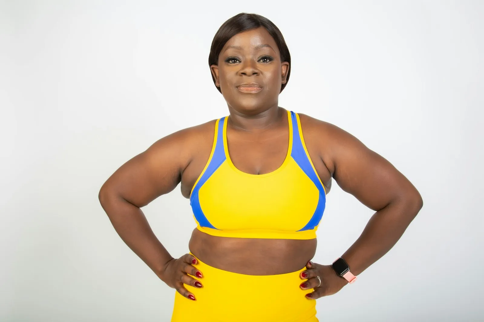 A smiling woman in a yellow sports bra and leggings