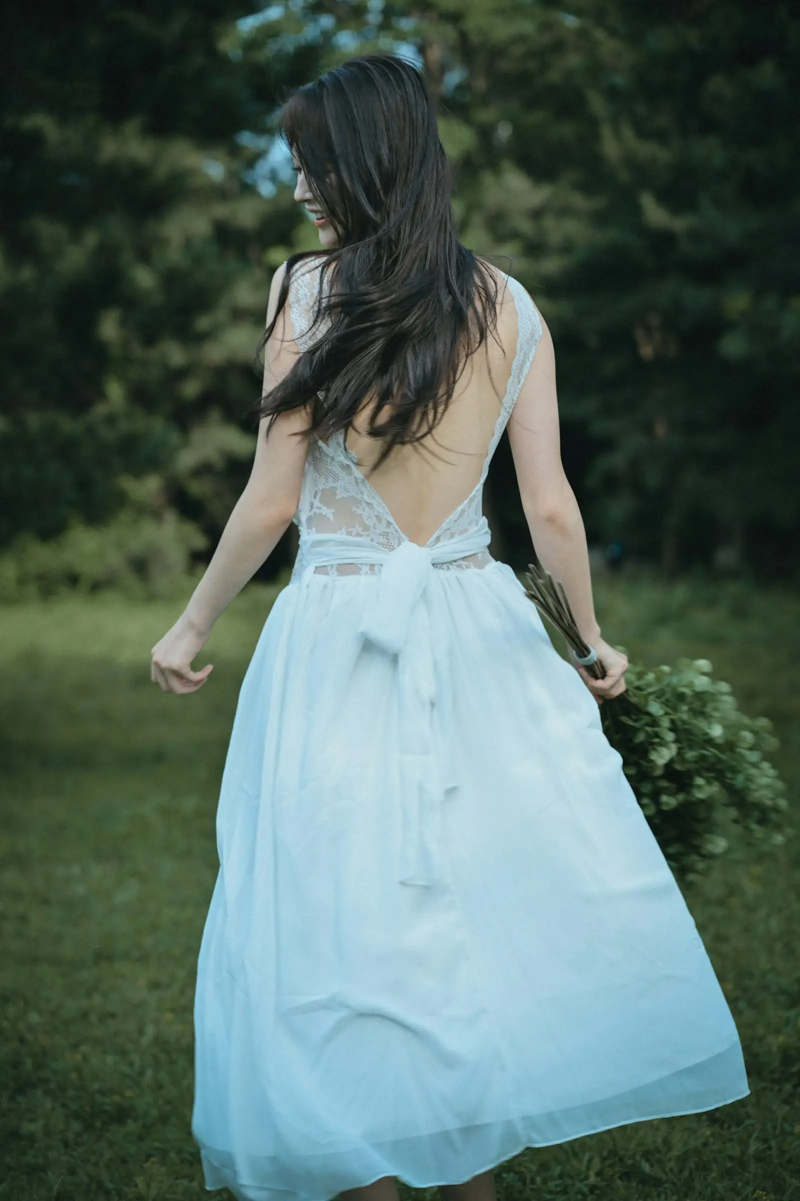 A woman in a pale blue backless dress walking through a garden