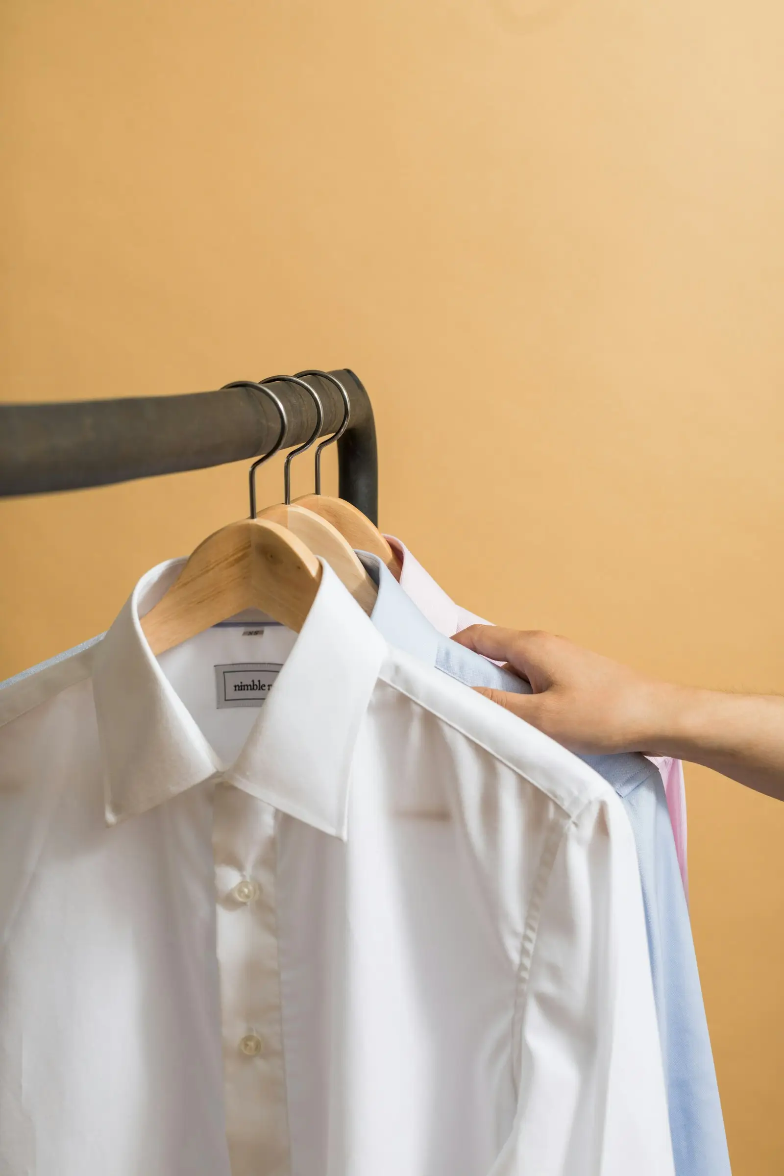 A hand choosing between white shirts hanging on a rail