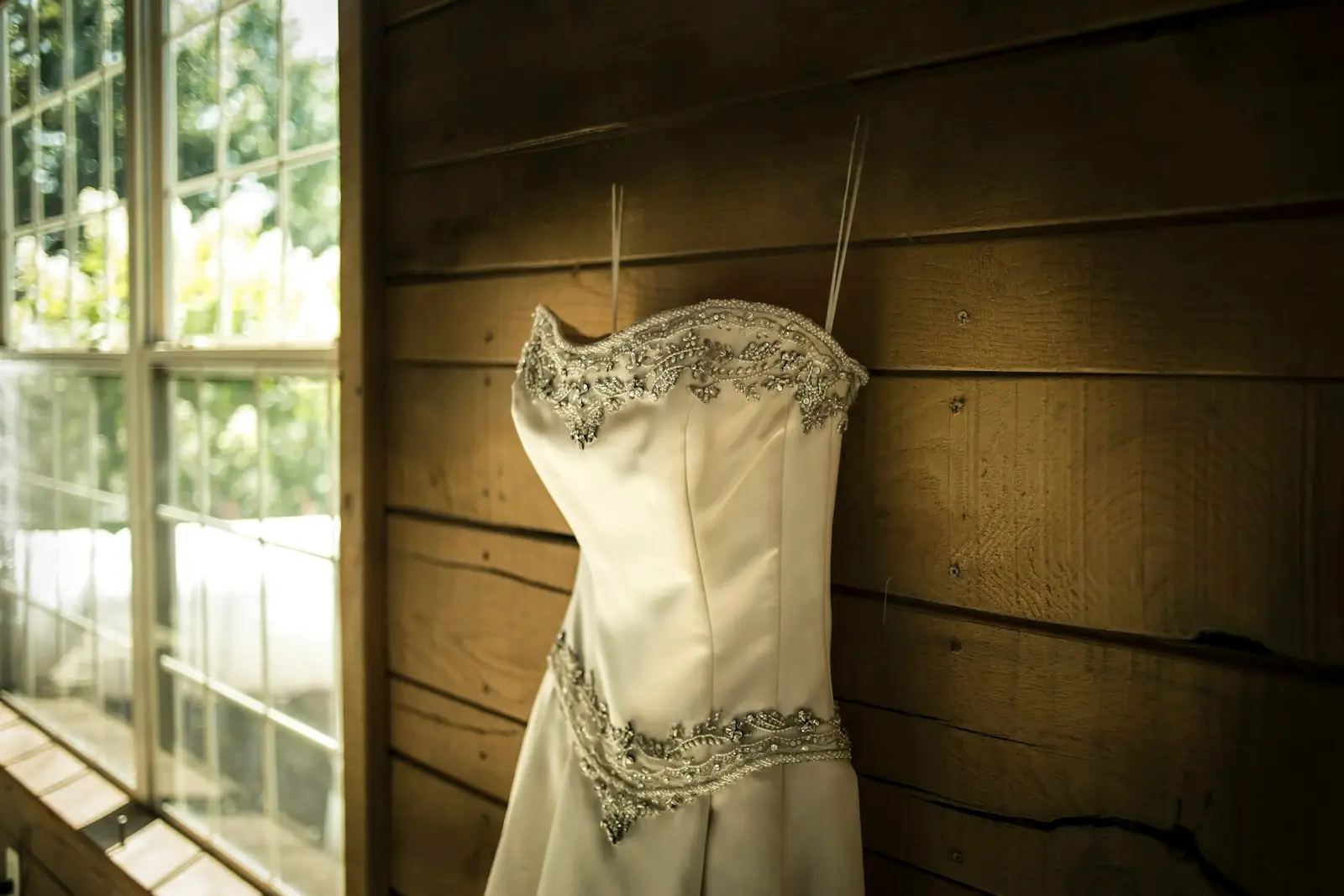A strapless ivory dress hanging by a window