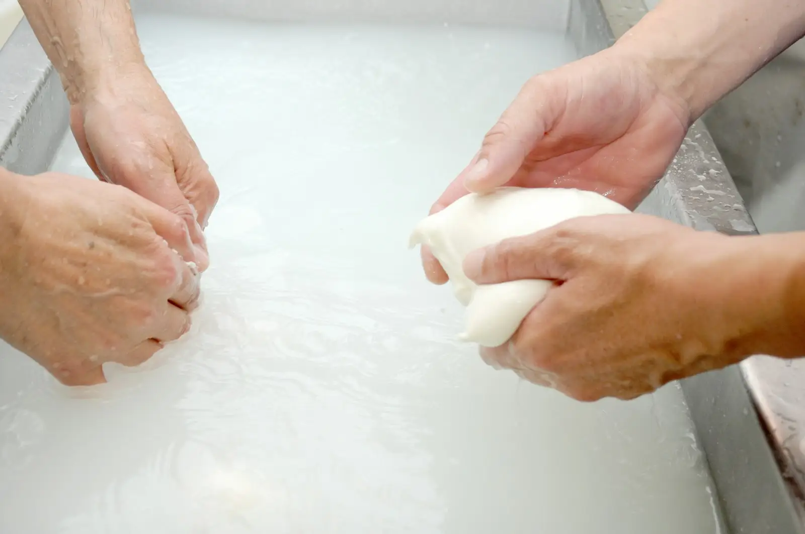 Hands washing a white garment in a basin of soapy water