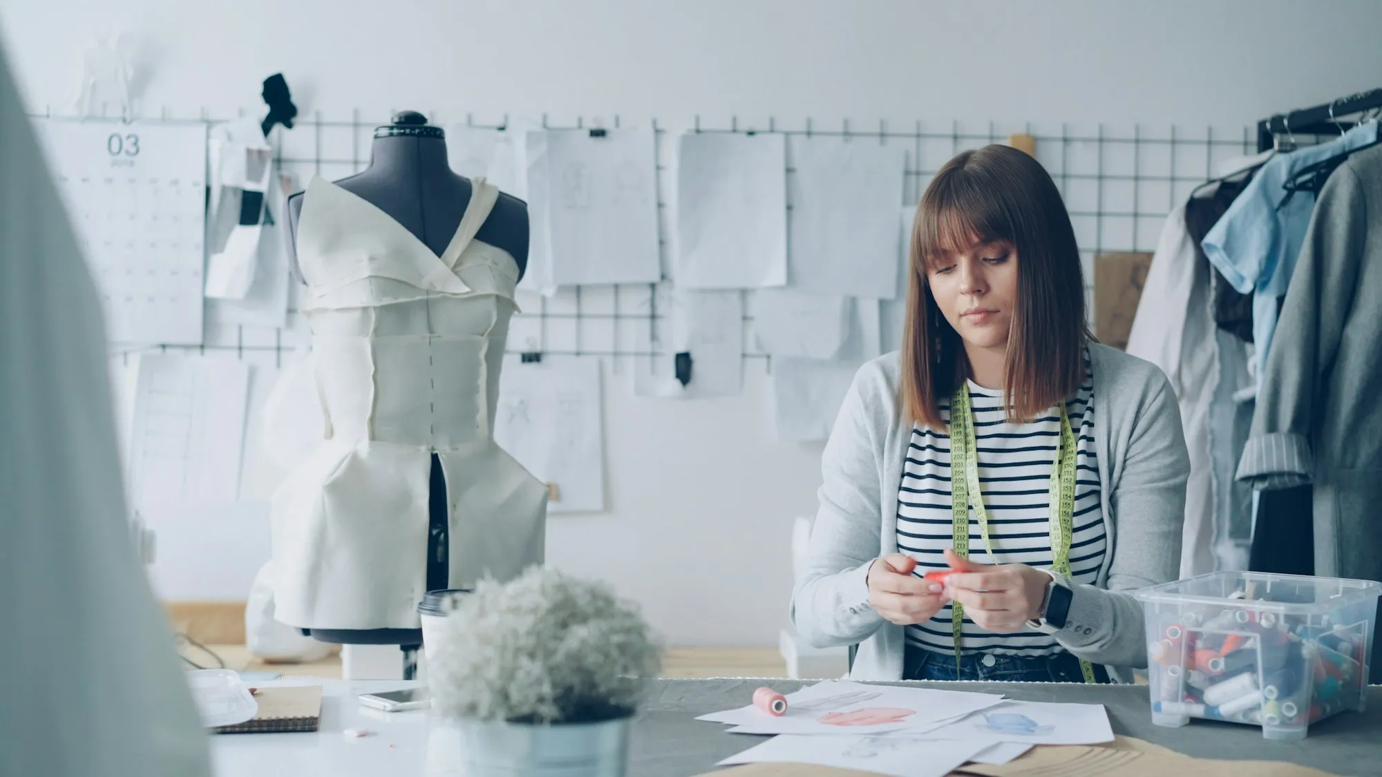 A fashion designer working at a table in a studio with a dress form and pattern sketches