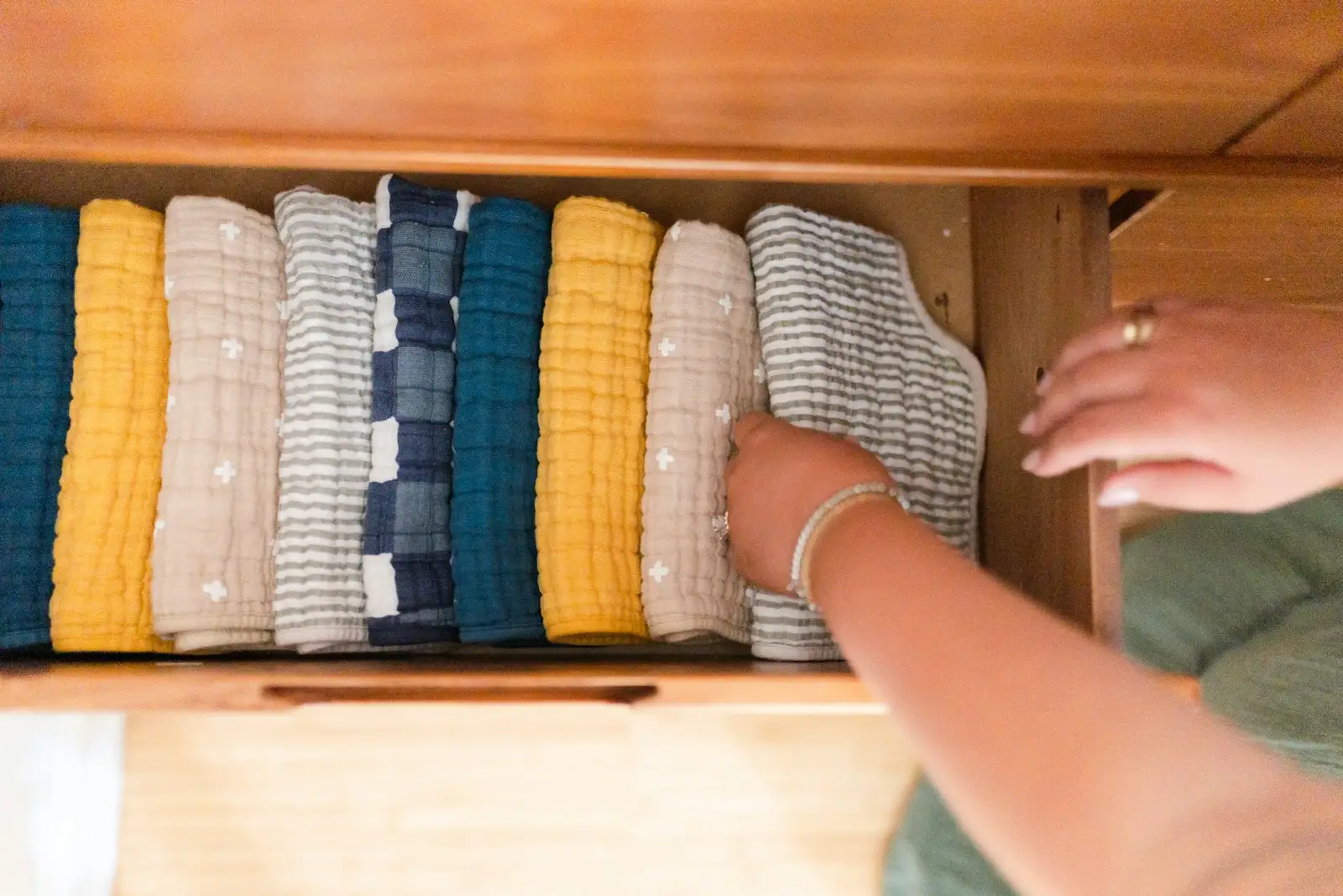 Hands arranging folded clothes in a wooden drawer