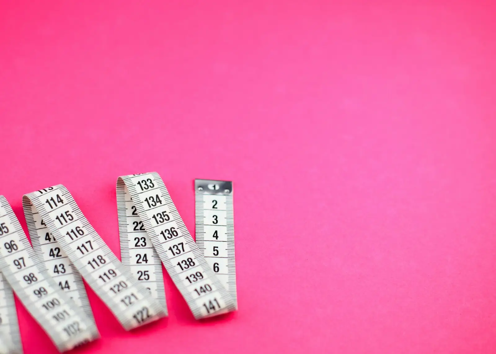 A measuring tape laid in loops on a pink background