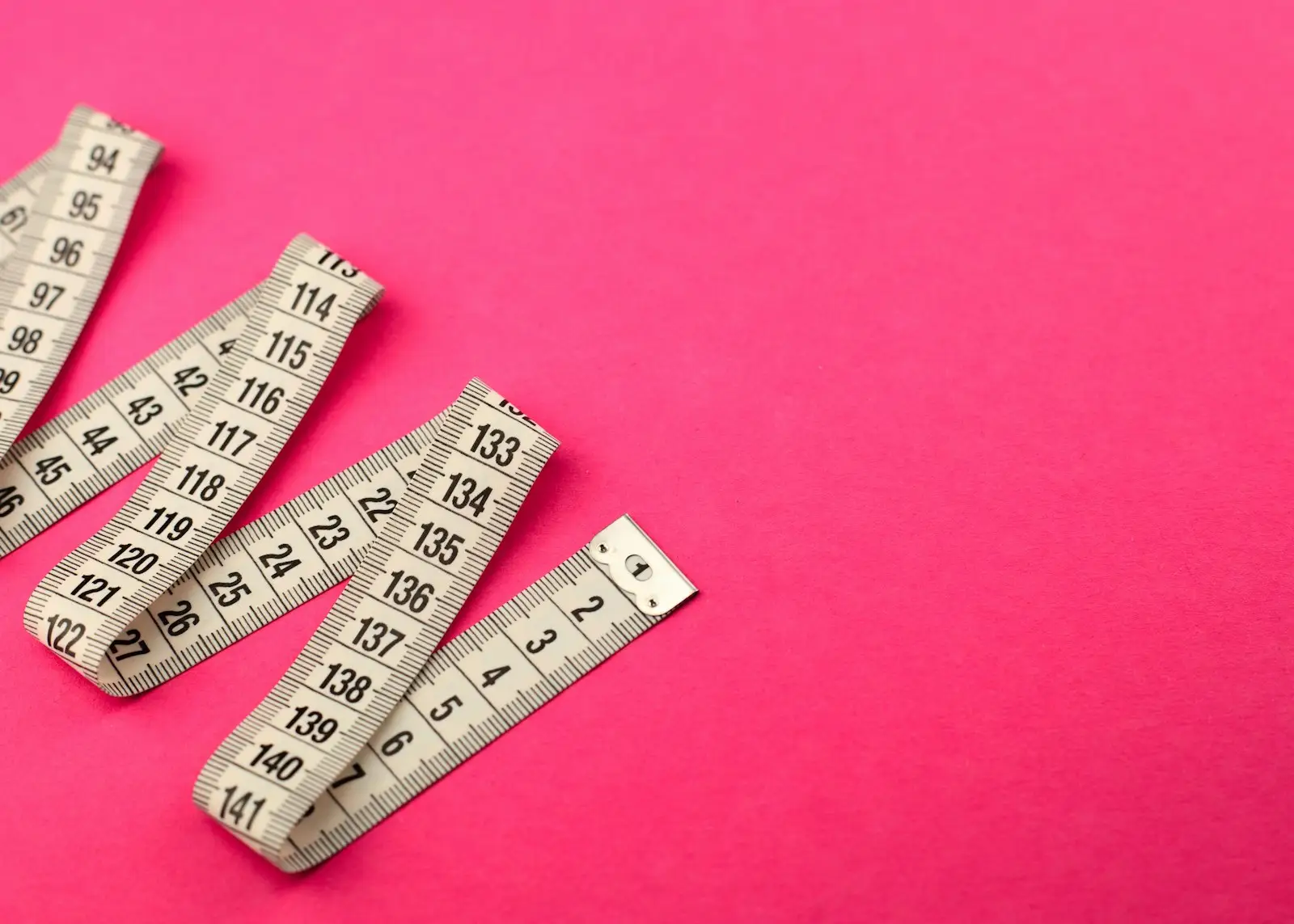 Folded measuring tapes on a bright pink background
