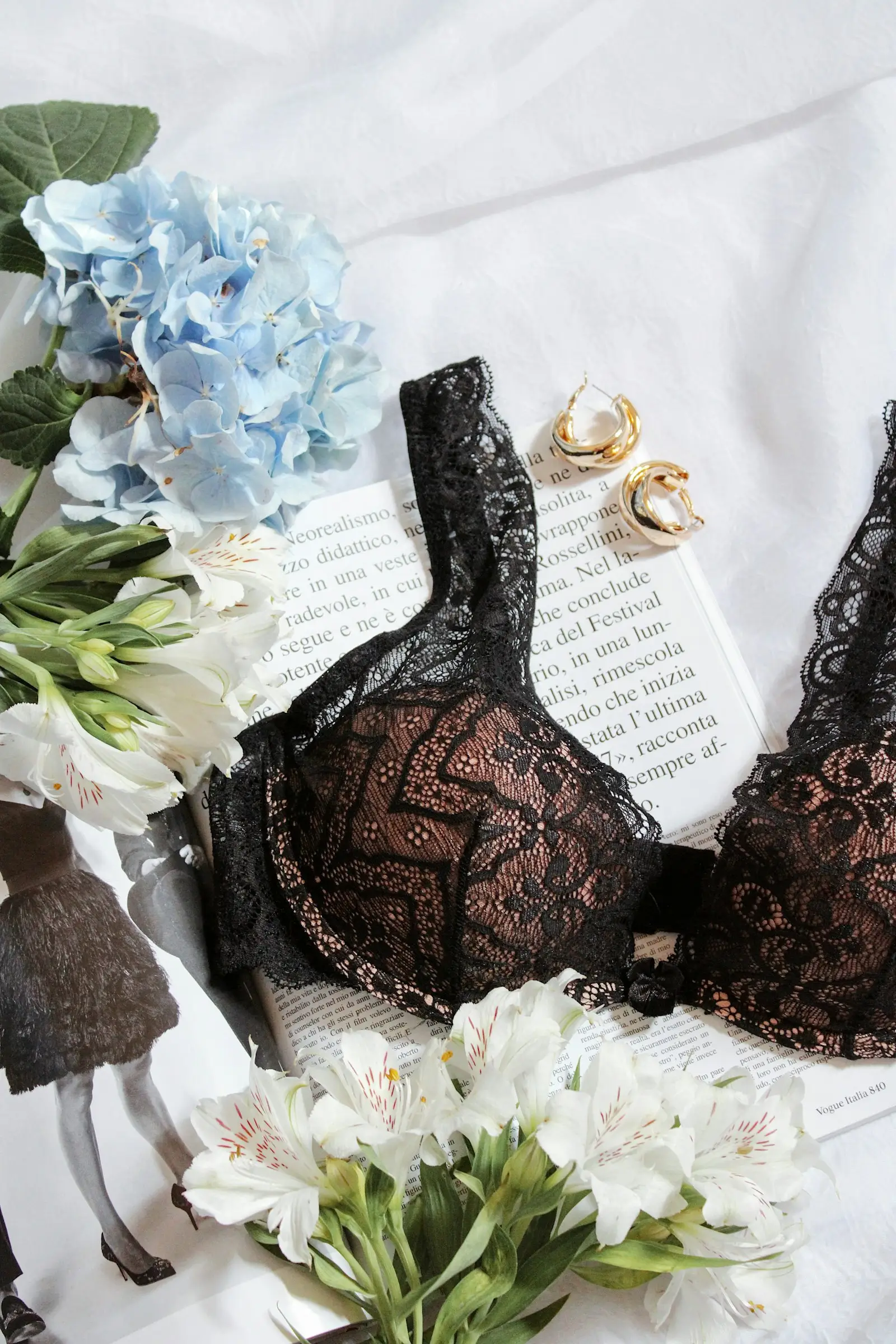 A black lace underwired bra on a table with flowers and an open book
