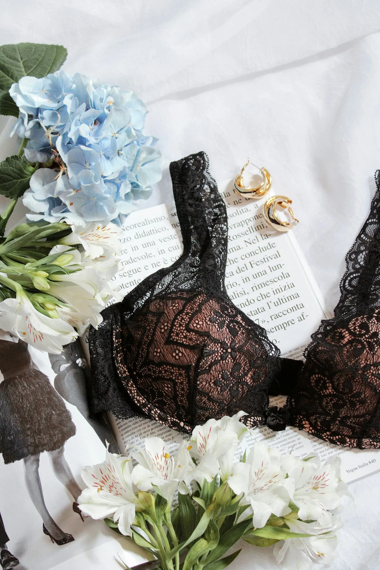 A black lace underwired bra on a table with flowers and an open book