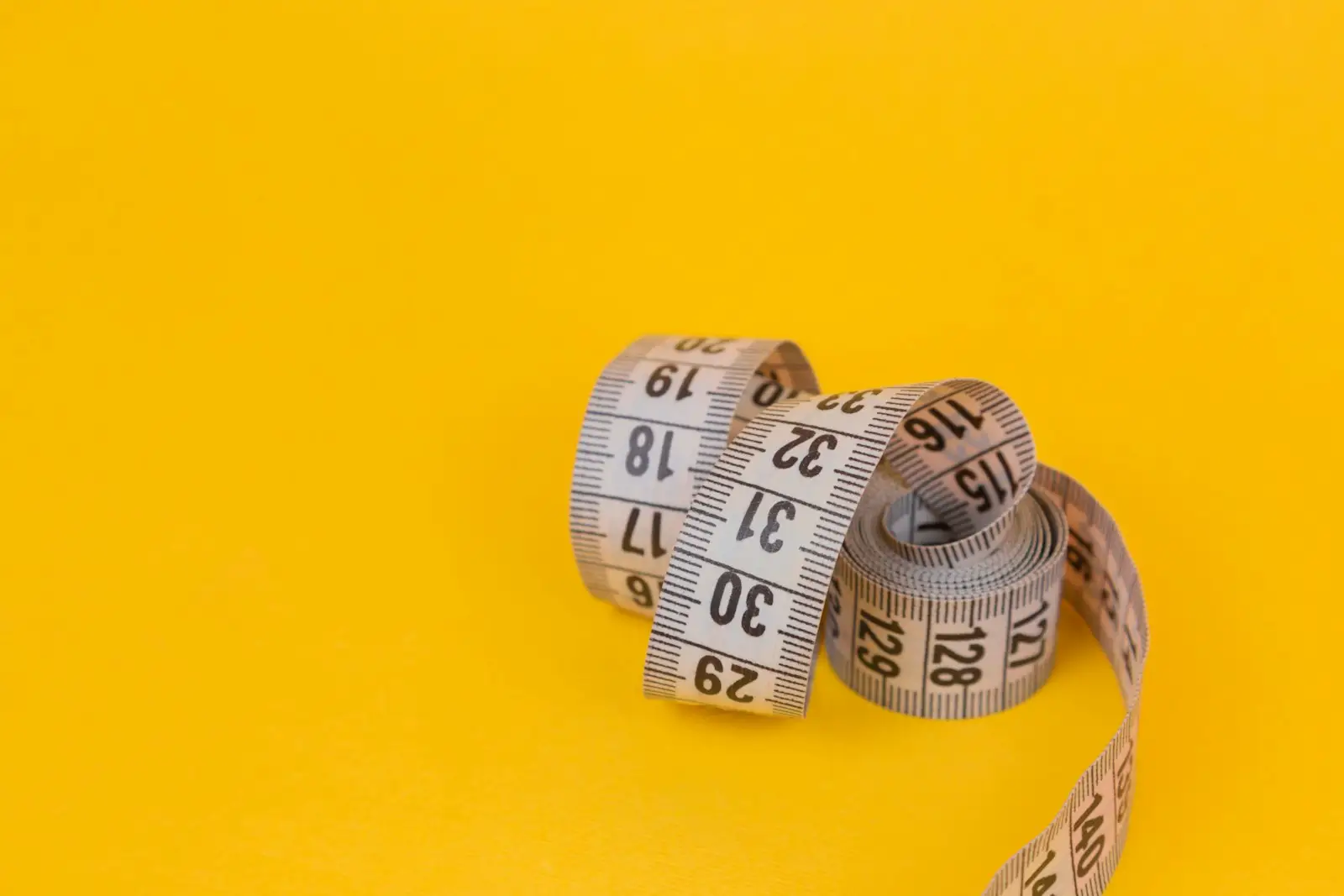 A coiled tailor’s measuring tape on a yellow background