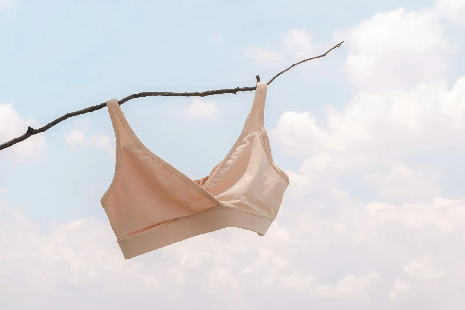 A soft beige wire-free bra hanging from a branch against the sky