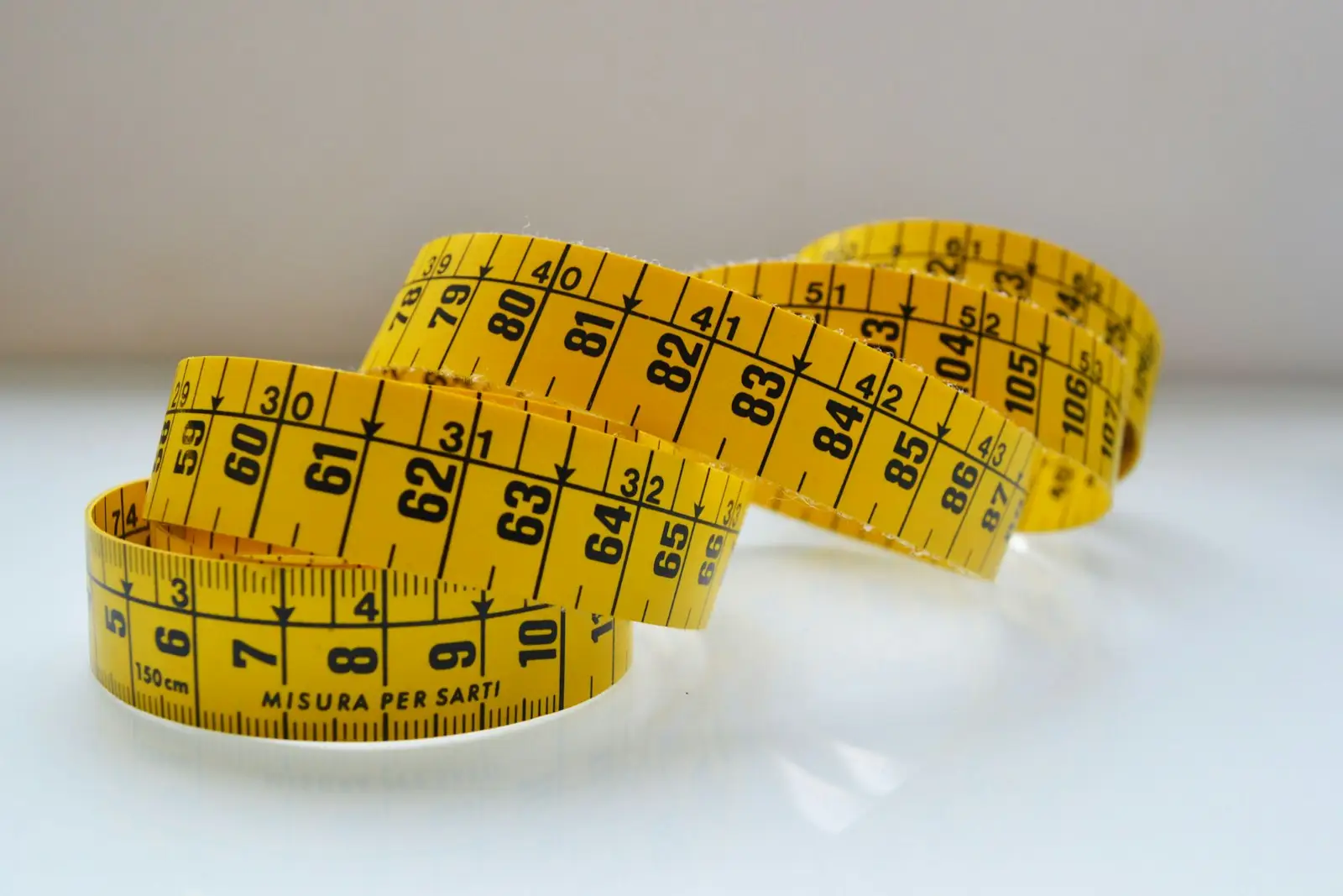 A yellow measuring tape loosely coiled on a white surface
