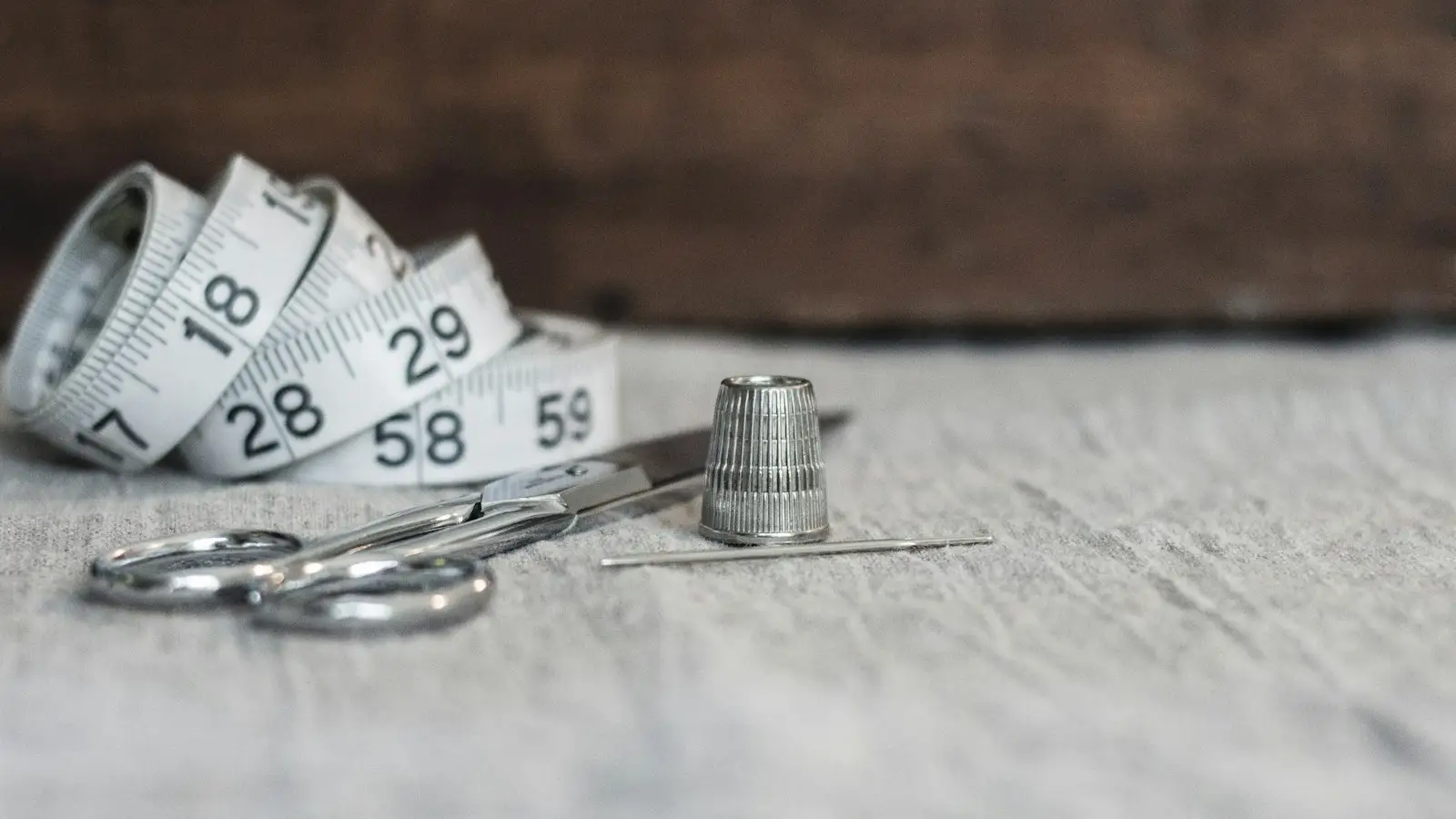 A measuring tape, scissors and thimble on a wooden table