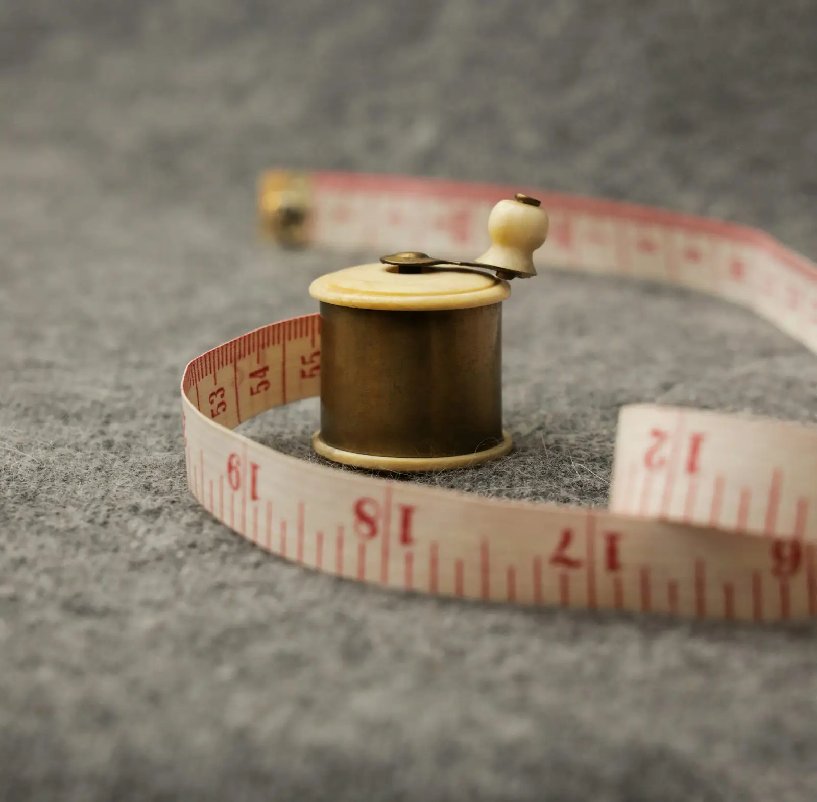 A cream measuring tape wrapped around a wooden spool of thread