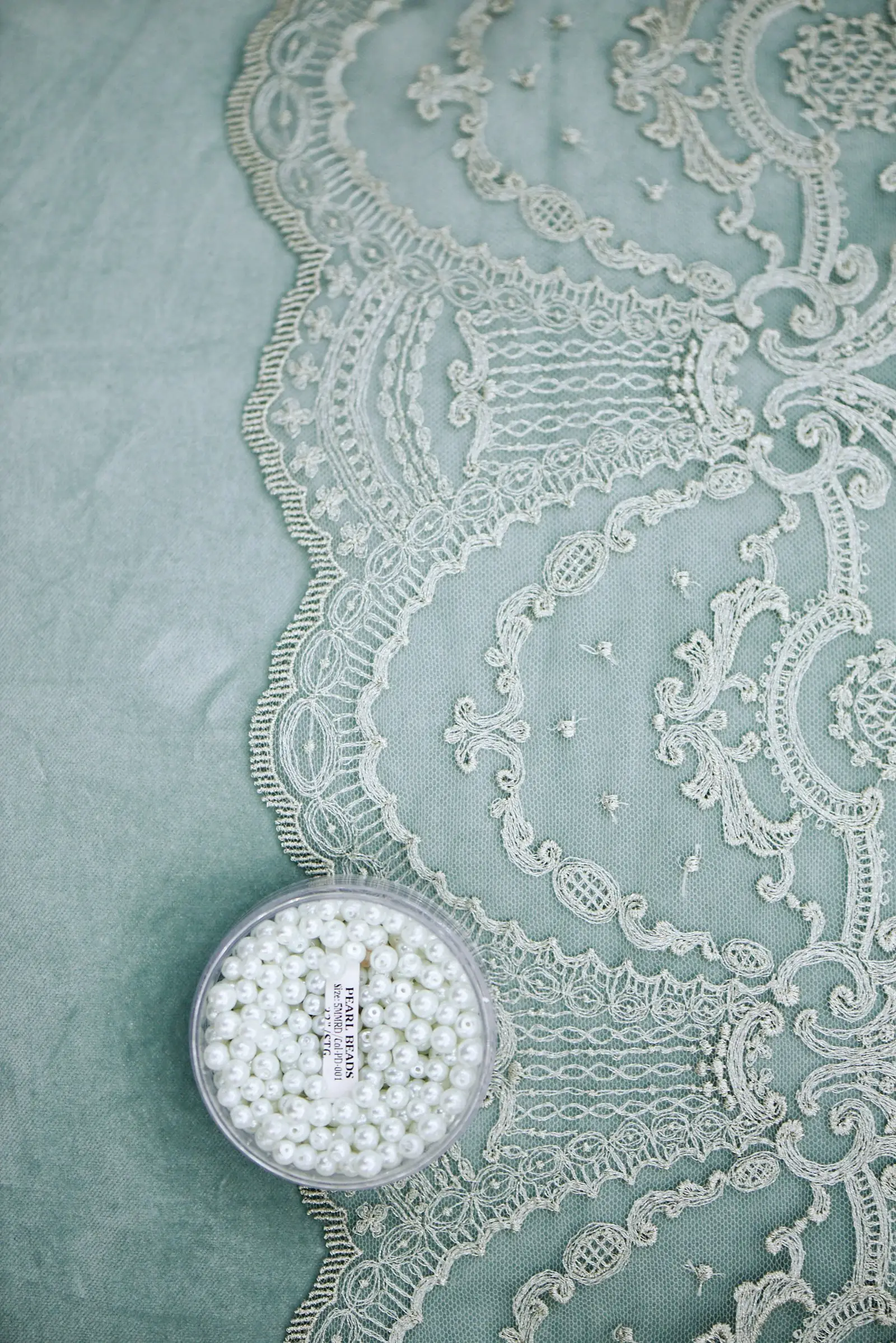 White embroidered lace and a dish of pearls on sage-green fabric
